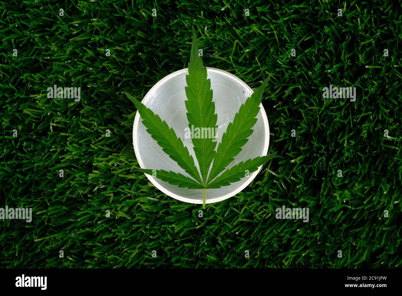 pot de crème blanche avec feuille de marijuana verte sur herbe verte. beauté, soins du corps cosmétiques avec extrait de cannabis. Banque D'Images