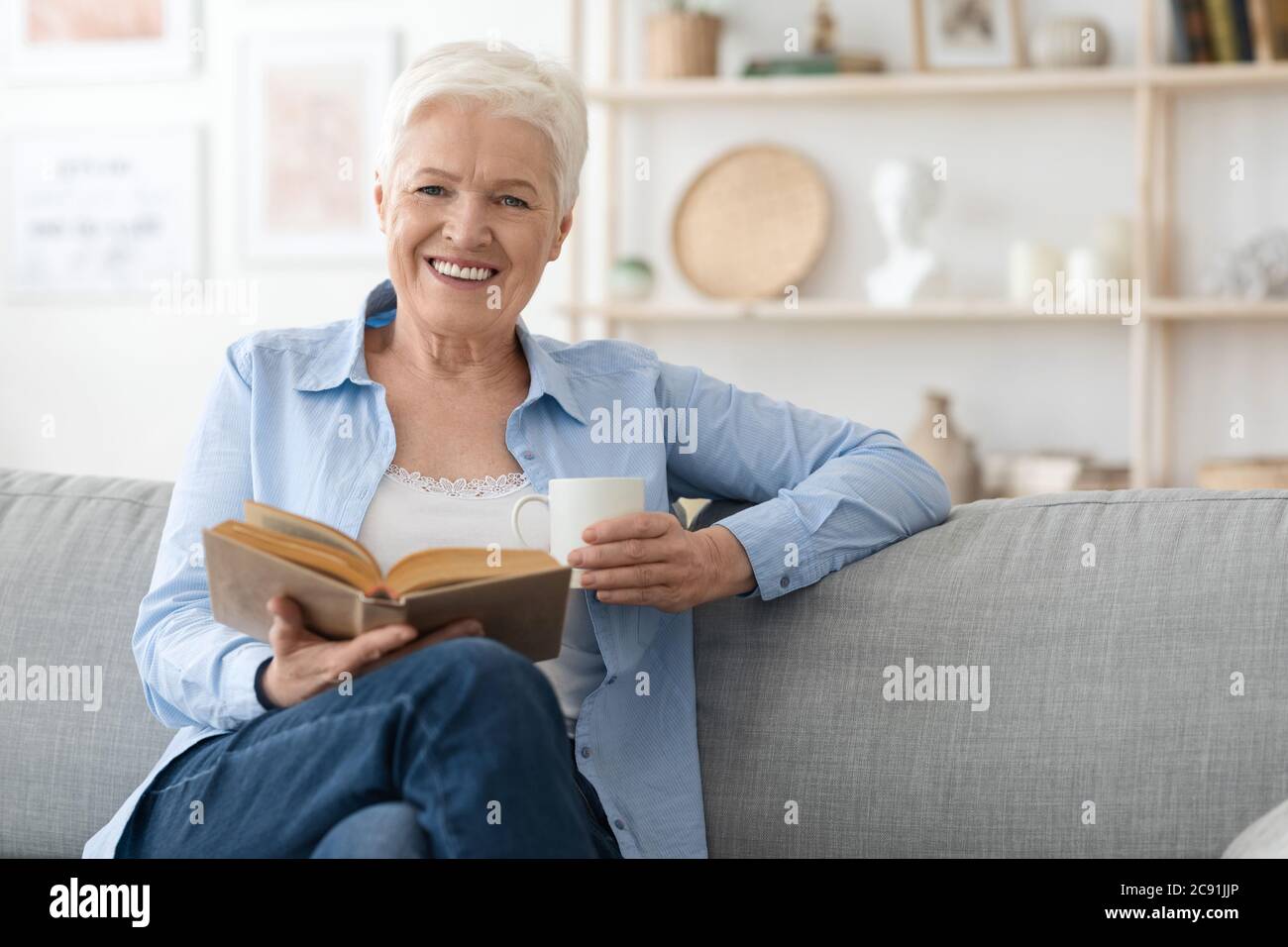 Livre Lover. Femme âgée souriante appréciant la lecture, se détendant sur le canapé à la maison Banque D'Images