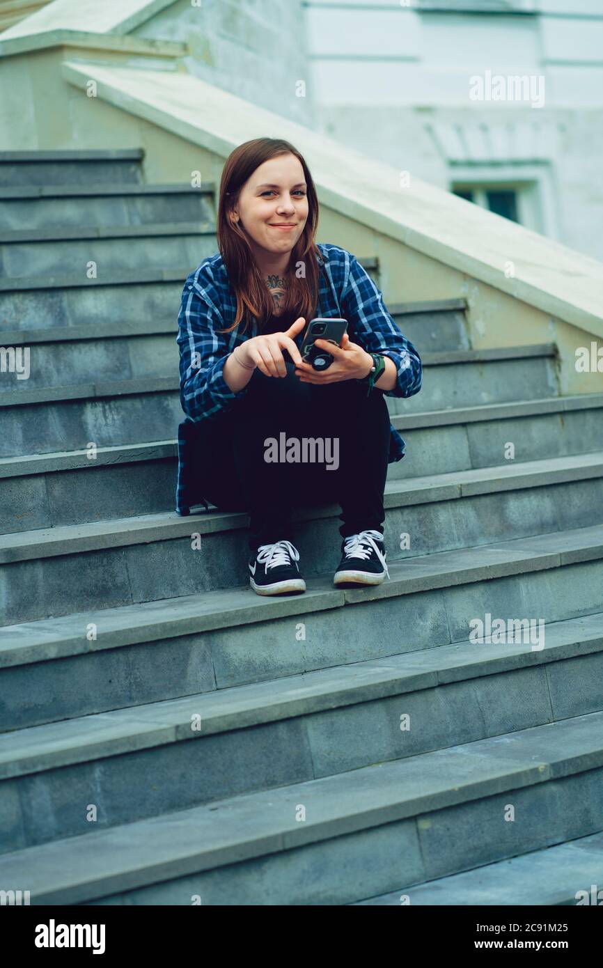 Jeune femme assise sur les escaliers du manoir avec un smartphone entre les mains. Femme adulte avec téléphone portable assise sur les marches du palais. Banque D'Images