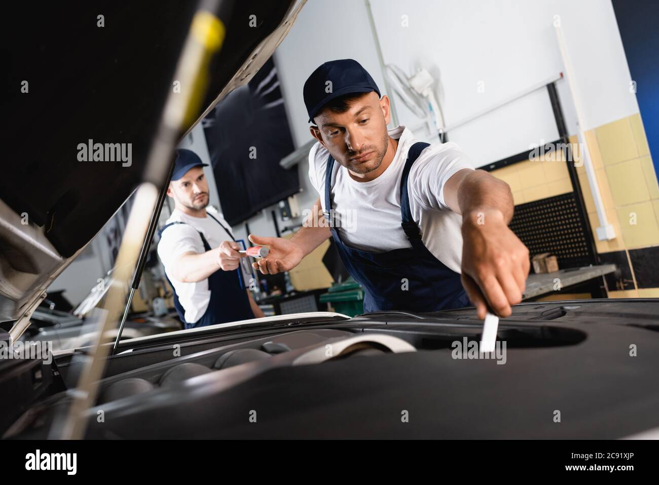 attention sélective du mécanicien dans le chapeau donnant un tournevis à un collègue de main qui répare la voiture dans l'atelier Banque D'Images