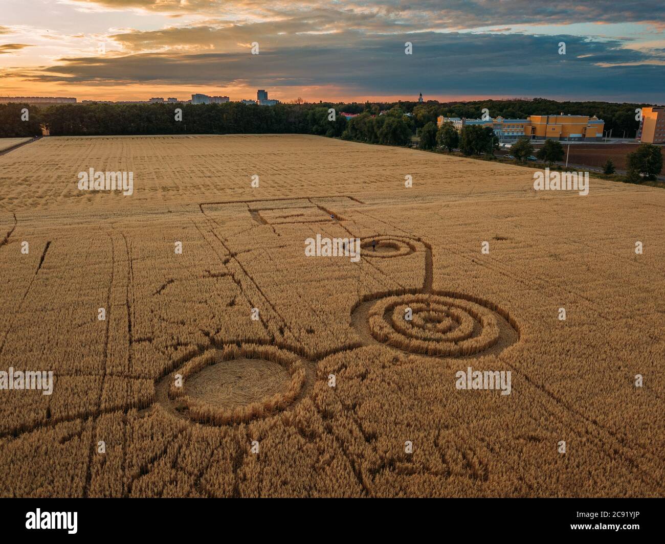 Mystérieux cercle de récolte dans champ d'avoine près de la ville à le coucher du soleil en soirée Banque D'Images