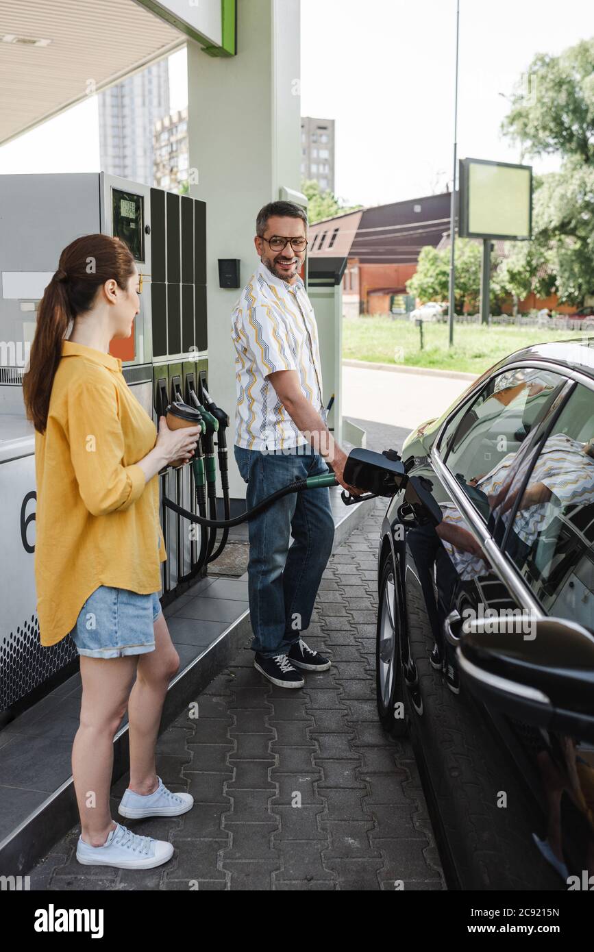 Attention sélective de sourire homme ravitaillant la voiture près de la femme avec le café pour aller à la station-service Banque D'Images