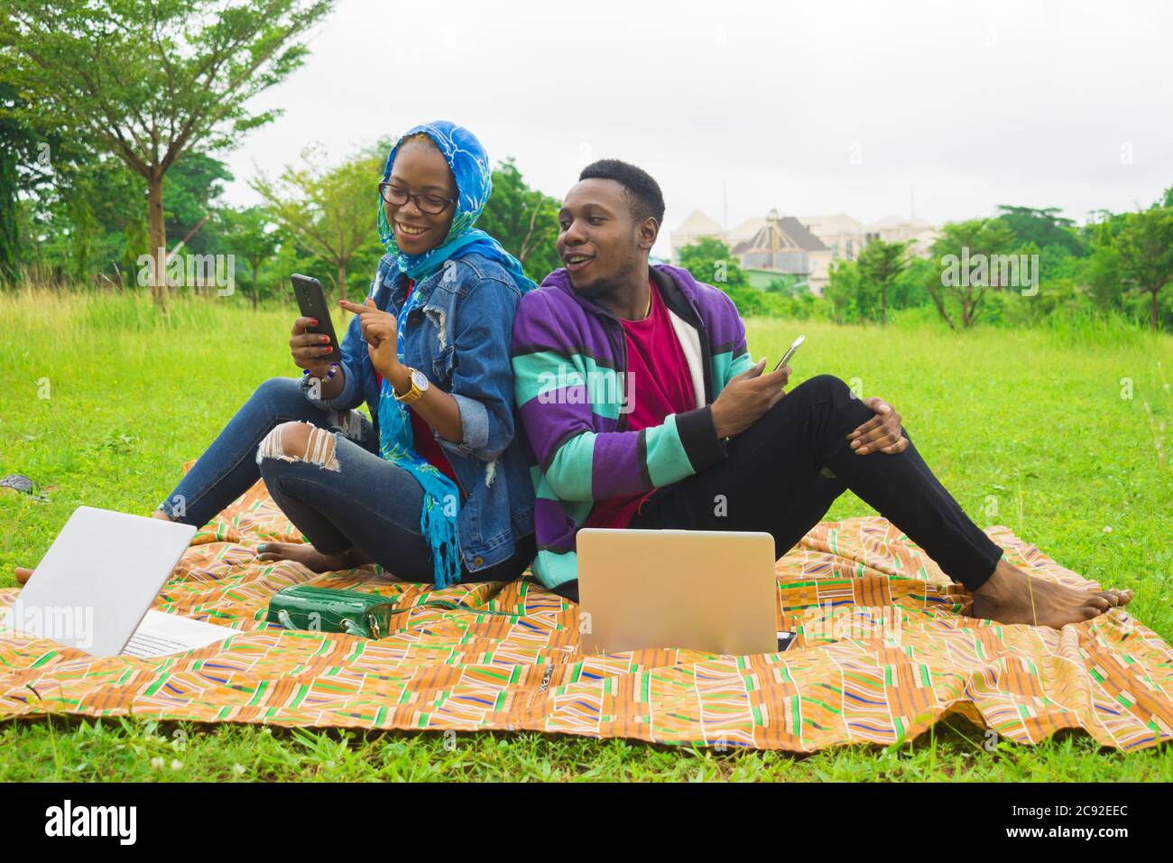 Heureux couple nigérian utilisant les téléphones portables pendant un pique-nique sur un pré recouvert d'herbe Banque D'Images