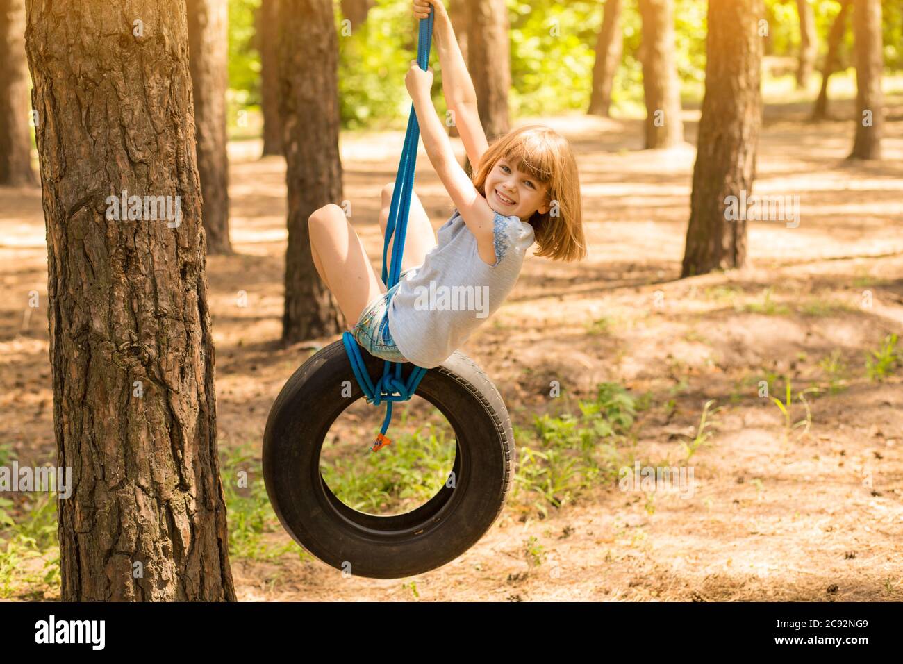 Bonne fille active jouant sur la roue pivotante dans la forêt le jour d'été ensoleillé. Activités de plein air en été pour les enfants. Enfant d'âge préscolaire s'amusant et Swingi Banque D'Images