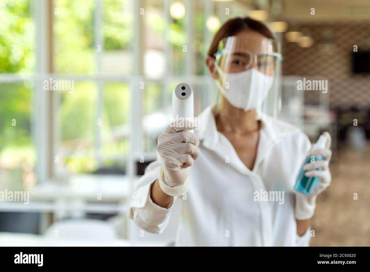 Portrait attrayant serveuse asiatique porter un masque et un masque facial tenir le thermomètre et l'assainisseur de gel d'alcool pour le nettoyage et l'hygiène avec le repos intérieur Banque D'Images