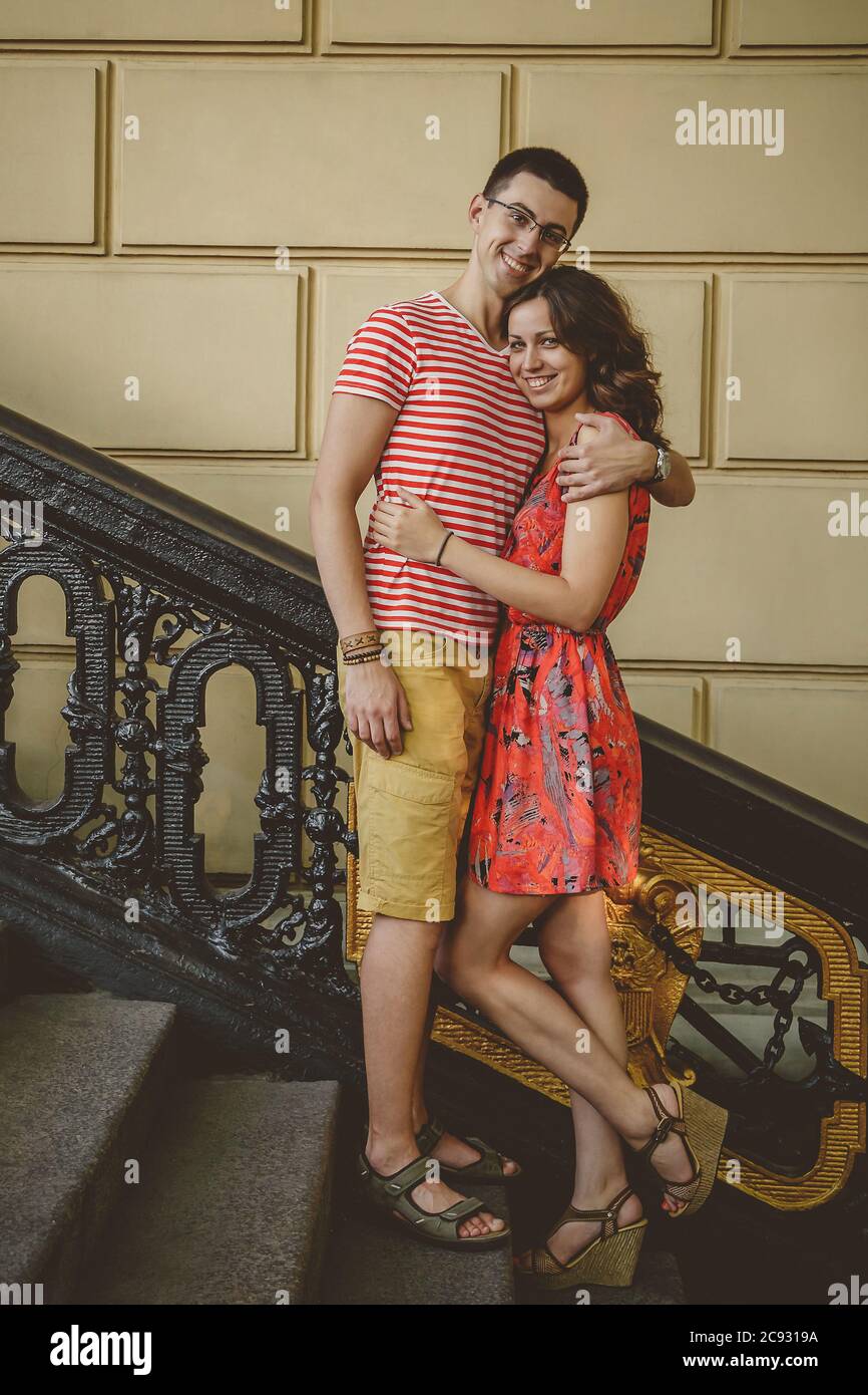 Beau jeune couple à l'extérieur dans des escaliers d'époque souriant et enveloppant, regardant la caméra Banque D'Images
