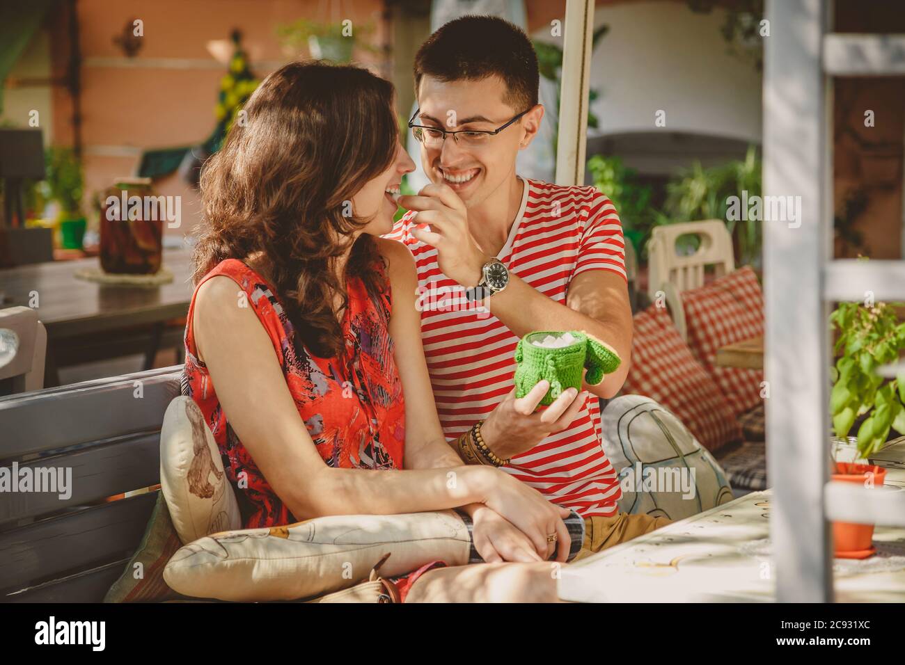 Jeune beau couple heureux aimant assis dans la rue café en plein air. Les hommes donnent des bonbons à sa petite amie. Début de l'histoire d'amour. Relation Banque D'Images