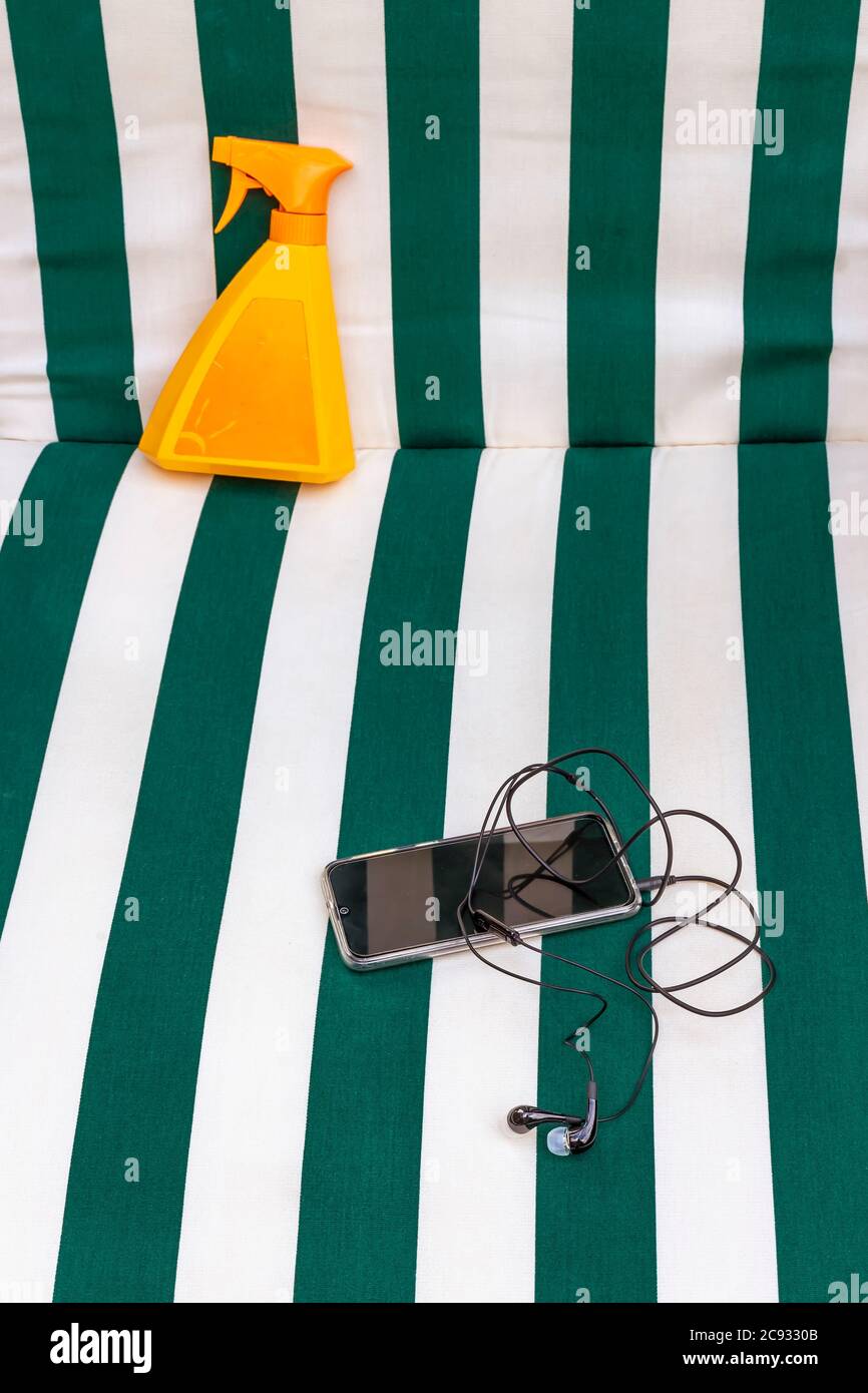 Un matelas de plage à rayures blanc et vert avec un spray solaire et un smartphone avec casque Banque D'Images