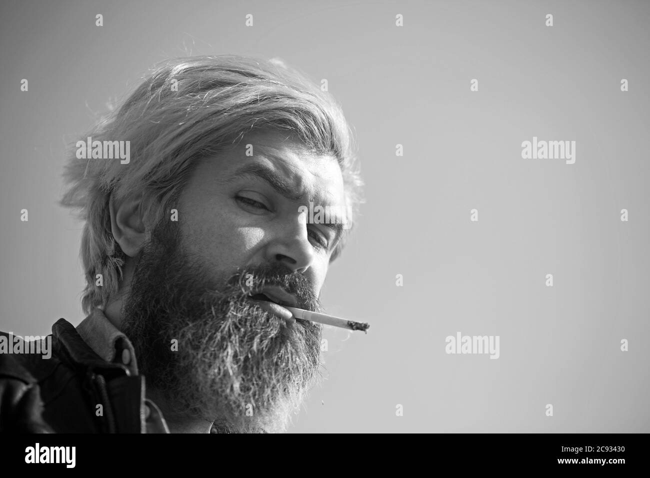 Homme barbu sérieux fuyant une cigarette sur la plage. Hipster barbu sur le ciel. Portrait en gros plan. Banque D'Images