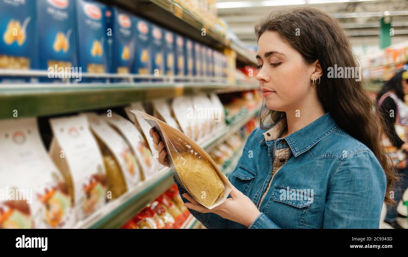 Shopping à l'épicerie. Une jeune belle femme tenant un paquet de pâtes. Dans les étagères d'arrière-plan avec les produits. Banque D'Images