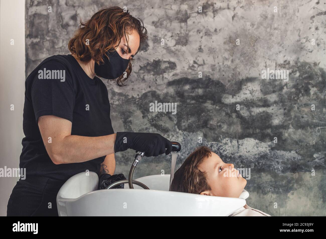 Joli coiffeur avec masque de protection noir et gants en latex préparant la  douche pour laver les cheveux d'un enfant Photo Stock - Alamy