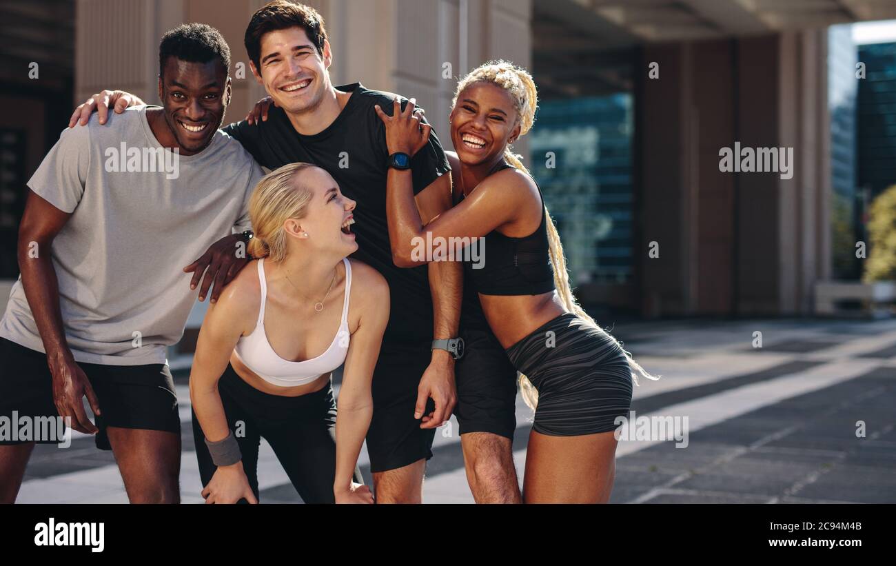Groupe d'hommes et de femmes posant pour une photo après avoir fait de l'exercice à l'extérieur. Des amis multiethniques s'amusent après une séance d'entraînement. Banque D'Images