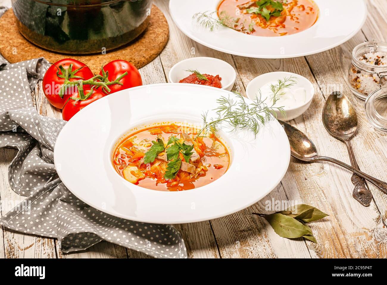 Cuisine traditionnelle ukrainienne ou russe. Assiette de soupe au chou, au bœuf, aux tomates fraîches et aux herbes sur fond de bois clair. Banque D'Images