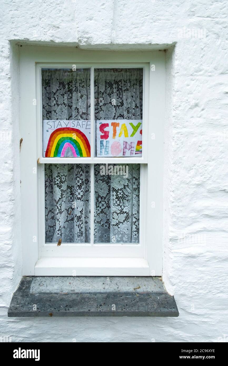 Un arc-en-ciel coloré dessiné à la main et un message pour rester à la maison affiché dans une fenêtre pendant la pandémie du coronavirus Covid 19. Banque D'Images