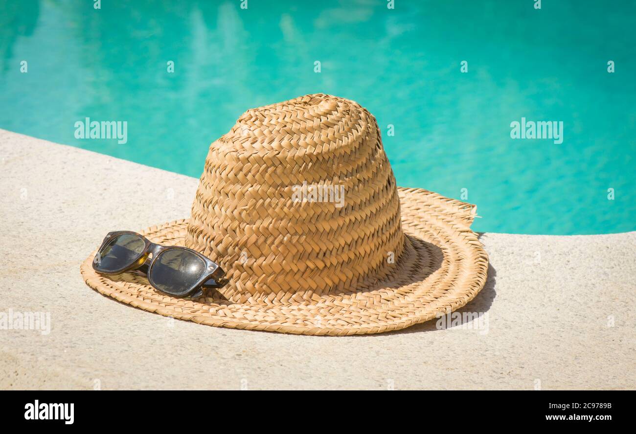 Chapeau de paille vintage avec lunettes de soleil à la frontière d'une piscine en été. Banque D'Images