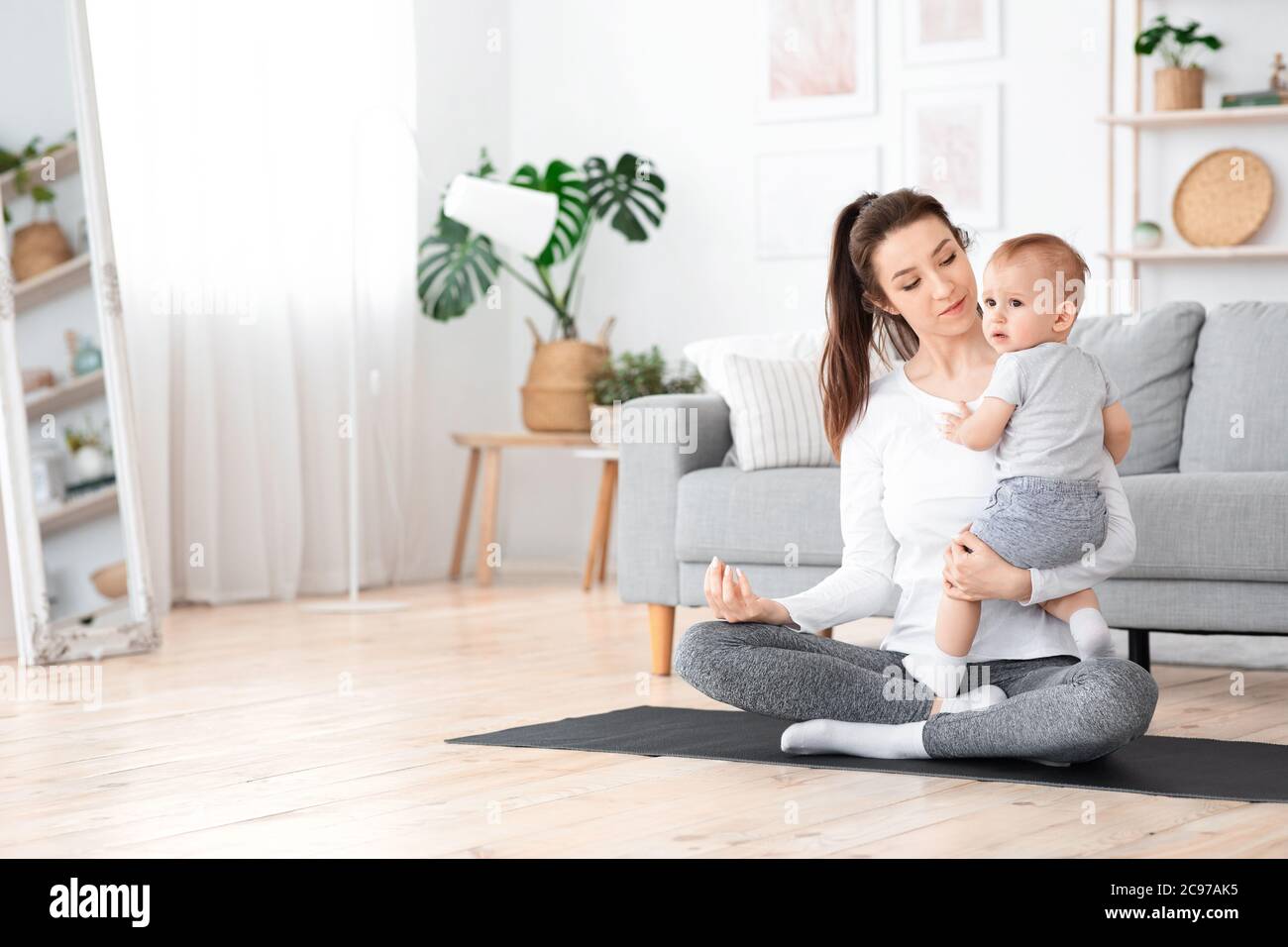 Jeune maman méditant avec bébé sur les bras, pratiquant le yoga à la maison Banque D'Images