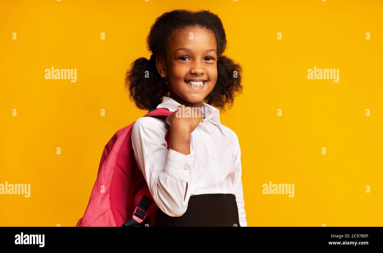 Fille d'école noire tenant sac à dos d'école souriant posant dans Studio Banque D'Images