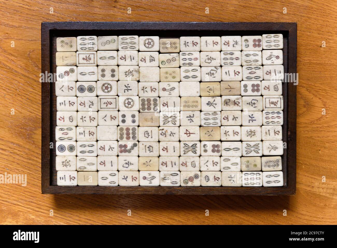 Top Down sur un jeu de mahjong vintage avec des tuiles soigneusement stockées avec le script chinois dans un tableau noir placé au centre sur une table en bois Banque D'Images
