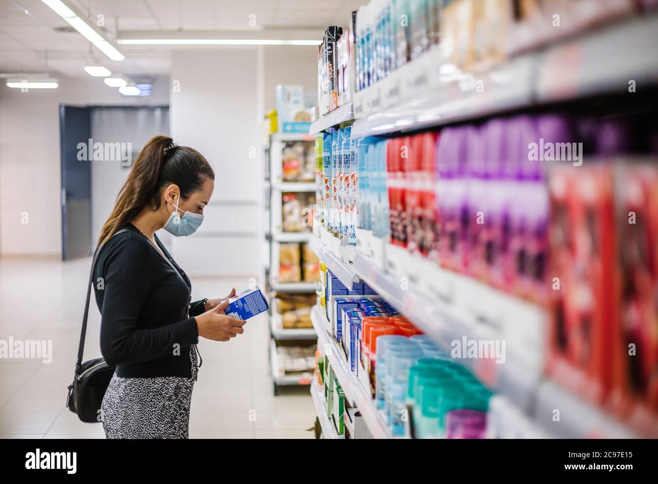 Une jeune femme portant un masque médical de protection lorsqu'elle fait ses courses dans un supermarché pendant une épidémie de coronavirus Banque D'Images
