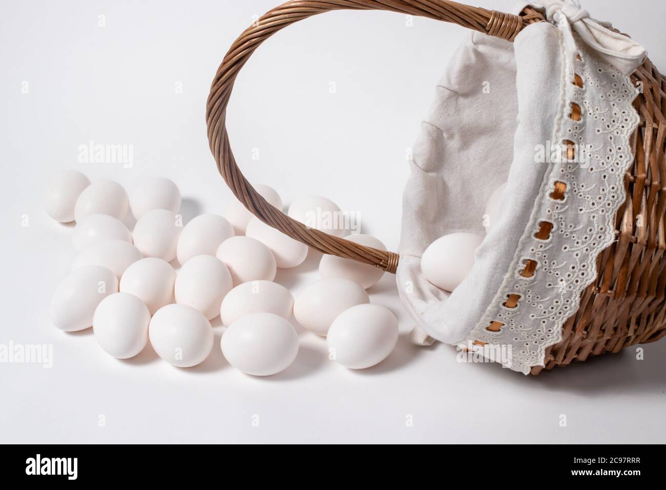 Beaucoup d'oeufs blancs de poulet dans un magnifique panier de brindilles en osier. De nombreux œufs ont été déversés du panier. Banque D'Images