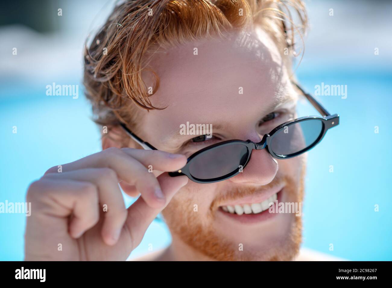 Gros plan de l'homme souriant aux cheveux rouges dans des lunettes de soleil Banque D'Images