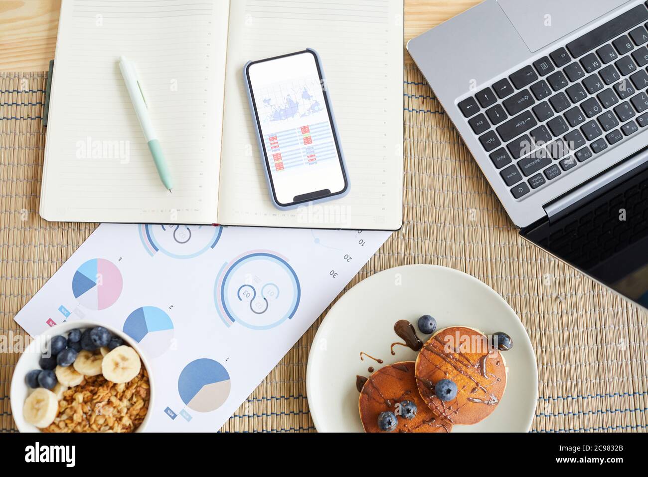 Vue en grand angle des documents professionnels avec graphiques et graphiques, ordinateur portable et petit déjeuner à la maison Banque D'Images
