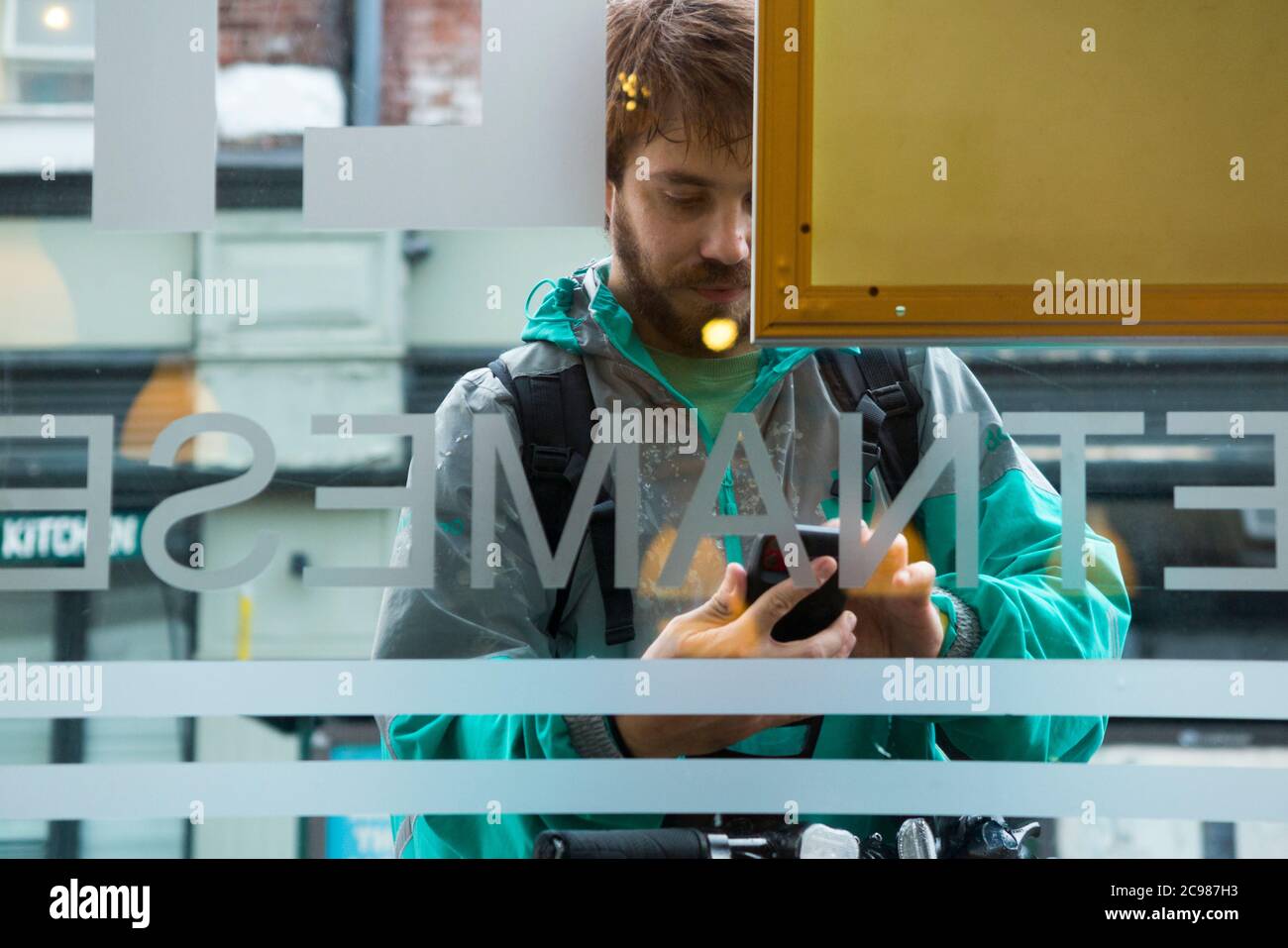 Deliveroo emporter repas courrier livraison cycliste à l'extérieur d'un restaurant d'où il fait une collection. Il vérifie son appareil mobile. Angleterre Royaume-Uni (120) Banque D'Images