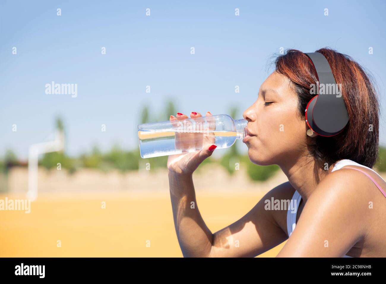 Gros plan de la femme qui boit de l'eau dans une bouteille en verre. Elle est à l'extérieur et porte un casque. Espace pour le texte. Concept de vie saine. Banque D'Images