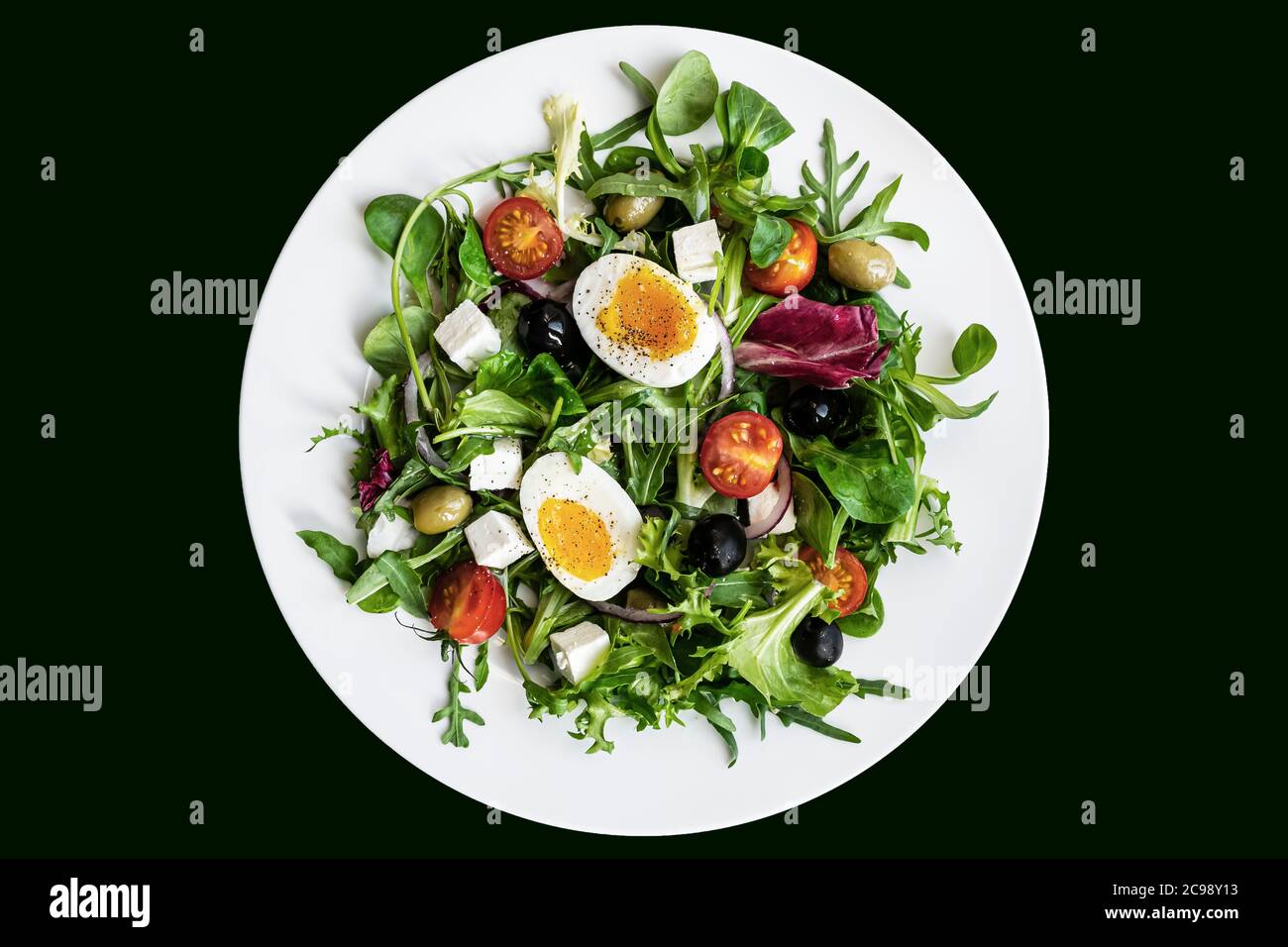Salade verte saine avec œuf dur, feta, olives, tomates cerises dans une assiette blanche sur fond noir. Flat lay, vue de dessus Banque D'Images