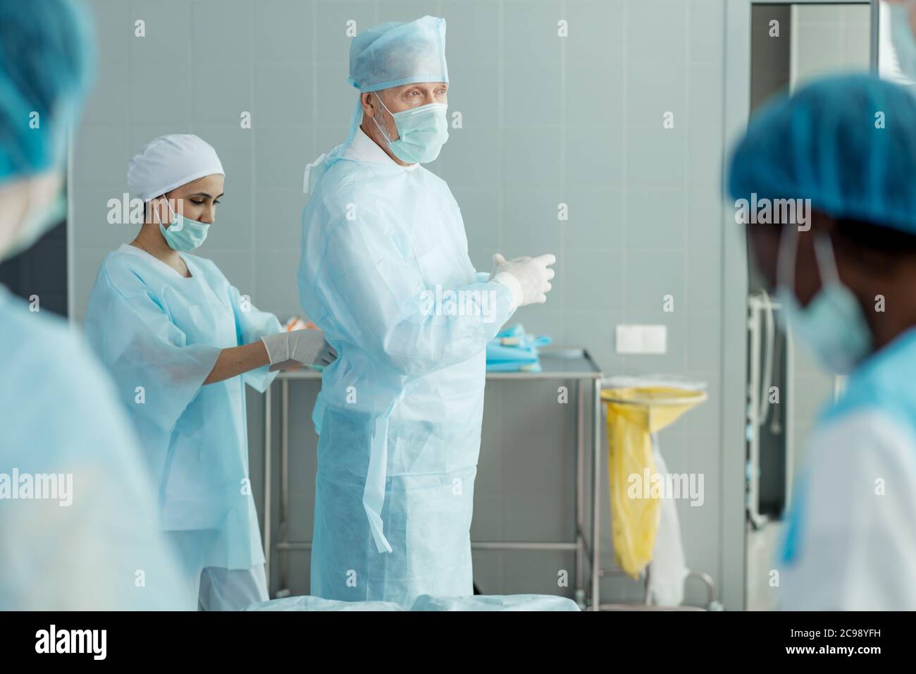 belle infirmière dans le masque et le chapeau aidant le médecin senior à mettre sur l'uniforme. gros plan photo rognée. Banque D'Images