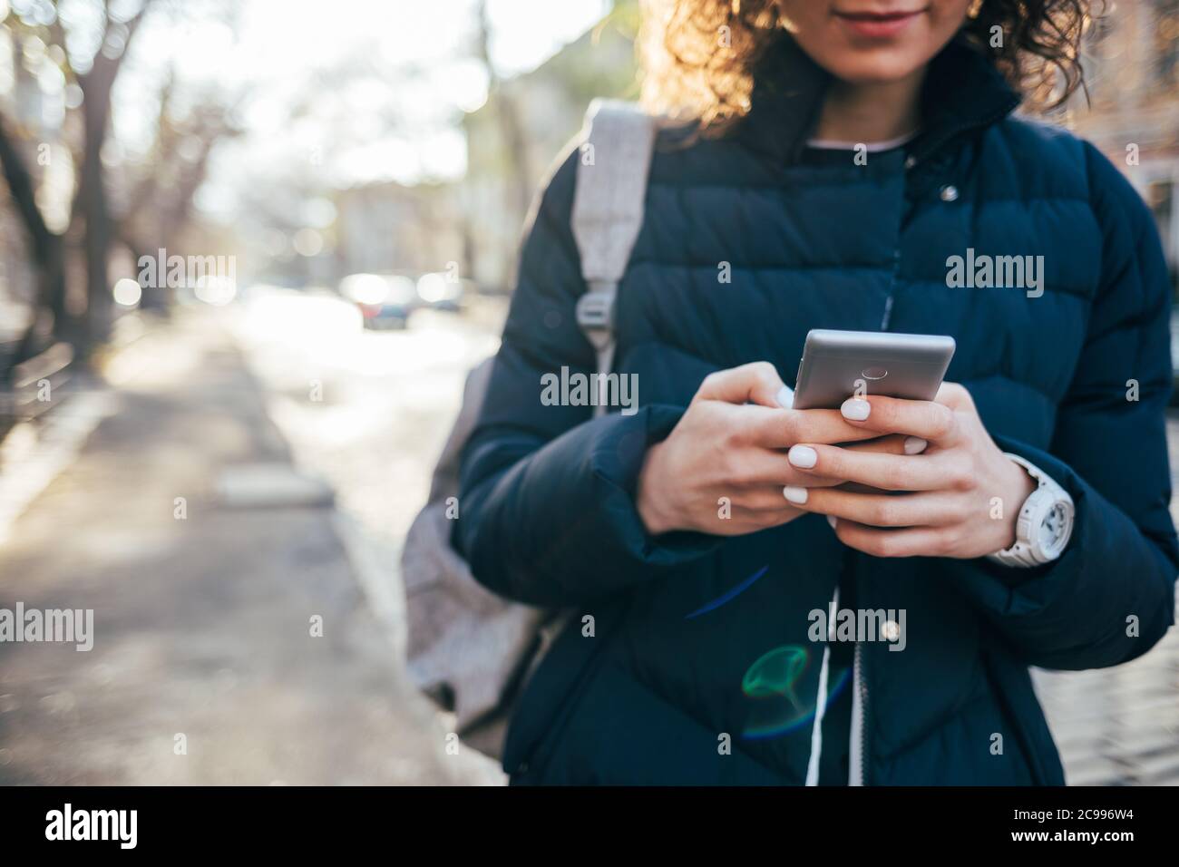Femme en blouson bleu dans la rue avec un téléphone portable entre ses mains Banque D'Images