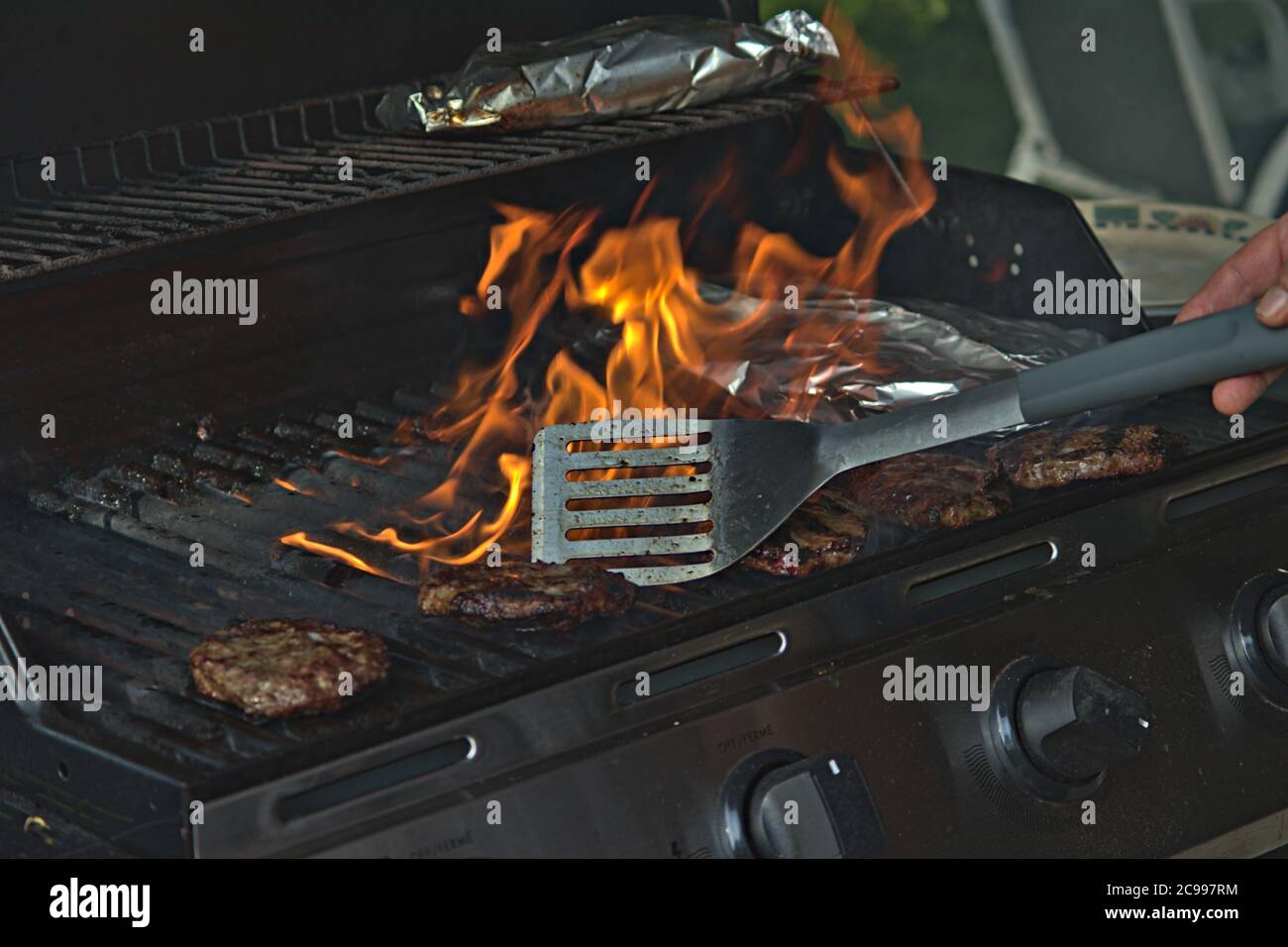 personne retournant des hamburgers sur le barbecue avec des flammes Banque D'Images