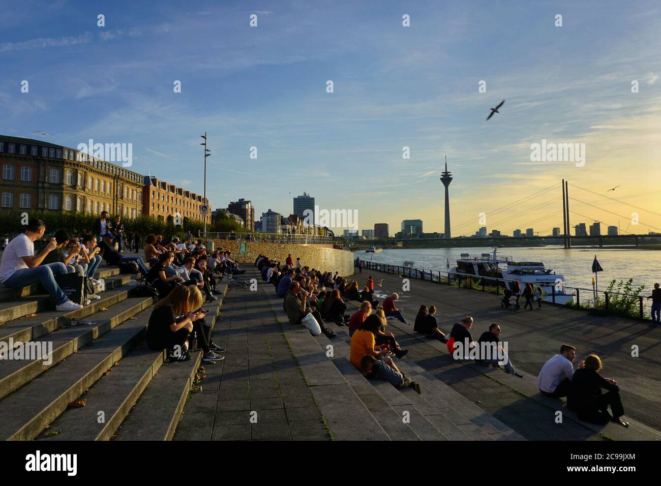 Personnes assises sur les marches de la terrasse du Rhin (Rheintreppe) à Burgplatz, le Rhin, et appréciant le coucher du soleil. Banque D'Images