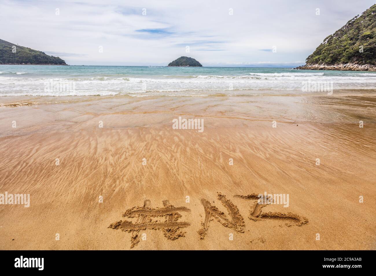 Mot NZ hashtag écrit dans le sable sur la plage de Nouvelle-Zélande pour les médias sociaux après le concept de publicité en ligne. Plage du parc national d'Abel Tasman, sud Banque D'Images