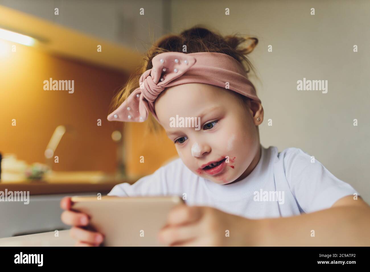 Fille mangeant à la table jouant au téléphone. Banque D'Images