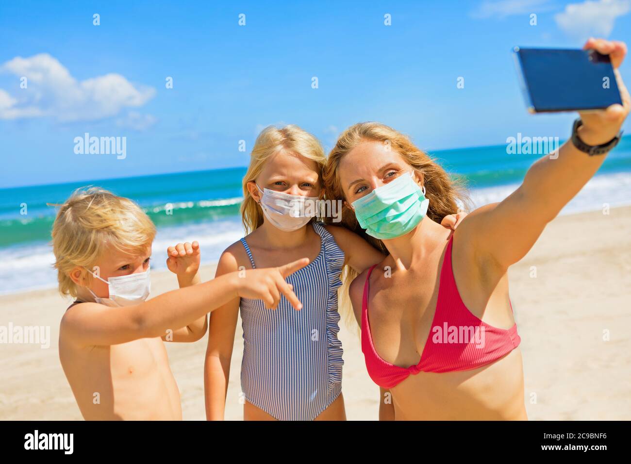 Drôle d'enfants avec la mère prenant photo selfie par smartphone sur la plage tropicale de mer. Règle de porter un masque de protection du visage dans les lieux publics en raison du coronavirus COVID Banque D'Images