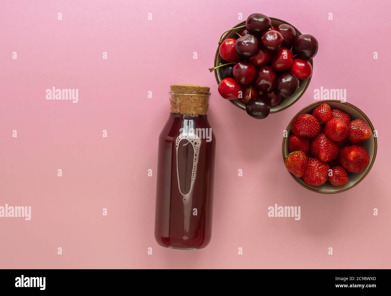 Jus de baies d'été dans une bouteille de verre avec cerise mûre et fraise Banque D'Images