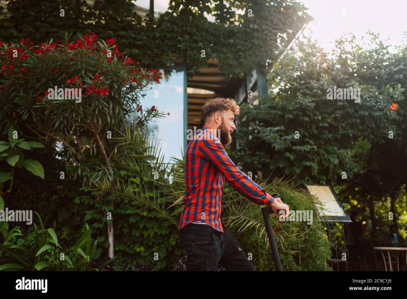 Vue latérale d'un jeune homme caucasien à barbe avec lunettes de soleil promenades sur la rue e scooter Banque D'Images