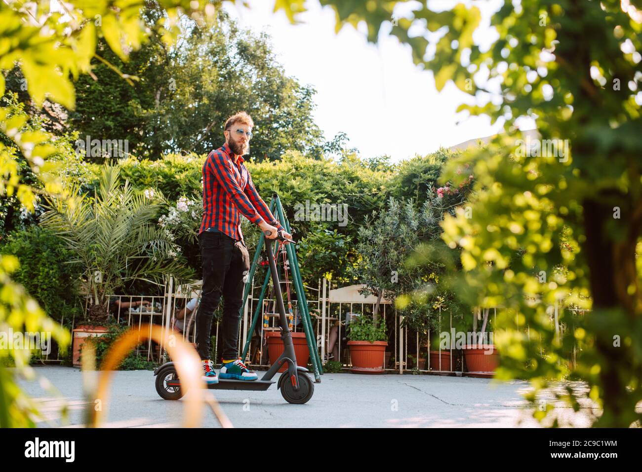 Vue latérale d'un jeune homme caucasien à barbe avec lunettes de soleil promenades sur la rue e scooter Banque D'Images