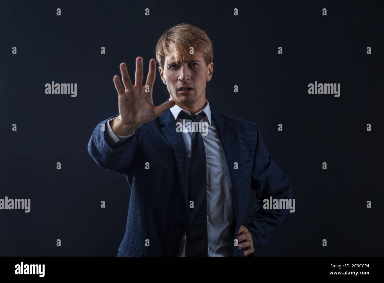 Arrêtez, un jeune homme d'affaires en costume et cravate fait un geste de protestation. Portrait dans le Studio sur un arrière-plan sombre. Banque D'Images