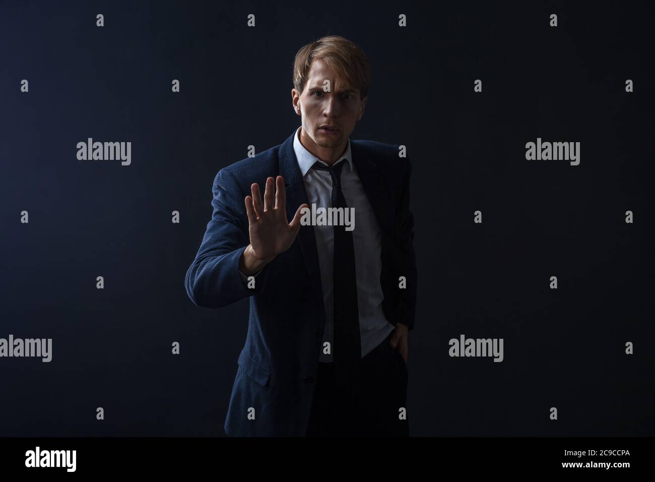 Arrêtez, un jeune homme d'affaires en costume et cravate fait un geste de protestation. Portrait dans le Studio sur un arrière-plan sombre. Banque D'Images