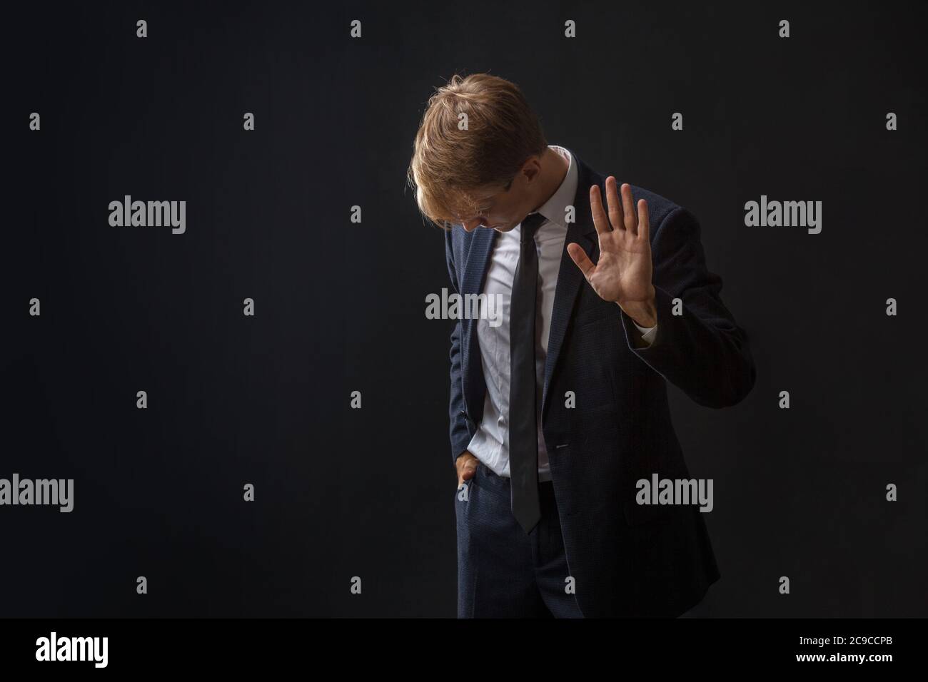 Arrêtez, un jeune homme d'affaires en costume et cravate fait un geste de protestation. Portrait dans le Studio sur un arrière-plan sombre. Banque D'Images