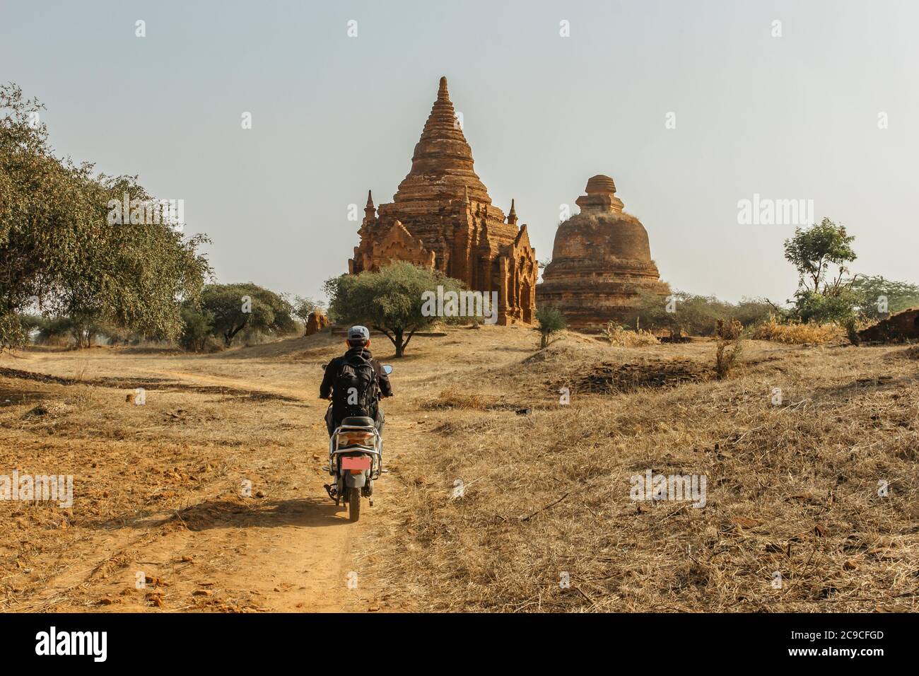 Homme à cheval sur un scooter électrique (e-bike) autour des vieux temples à Bagan, Myanmar. Pagodes et flèches des temples du site du patrimoine mondial de Baga Banque D'Images