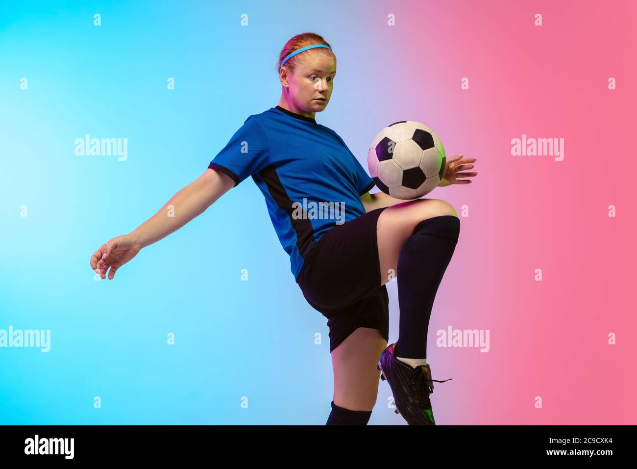 Balle rebondissante. Football féminin, entraînement de joueur de football en action isolé sur fond de studio de gradient dans la lumière du néon. Concept de mouvement, d'action, d'ahievements, de mode de vie sain. Culture de la jeunesse. Banque D'Images