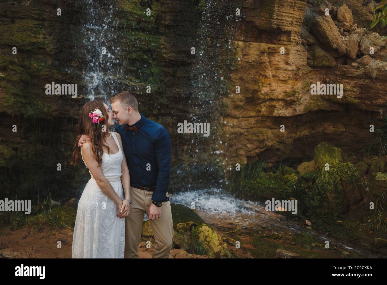 Cérémonie de mariage en plein air, marié souriant et mariée sont embrasser et embrasser devant une petite cascade Banque D'Images