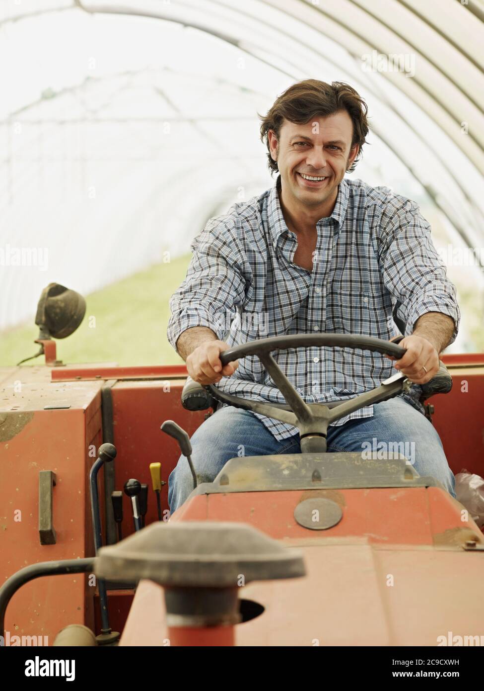 Portrait de l'agriculteur masculin conduisant un tracteur agricole et souriant Banque D'Images