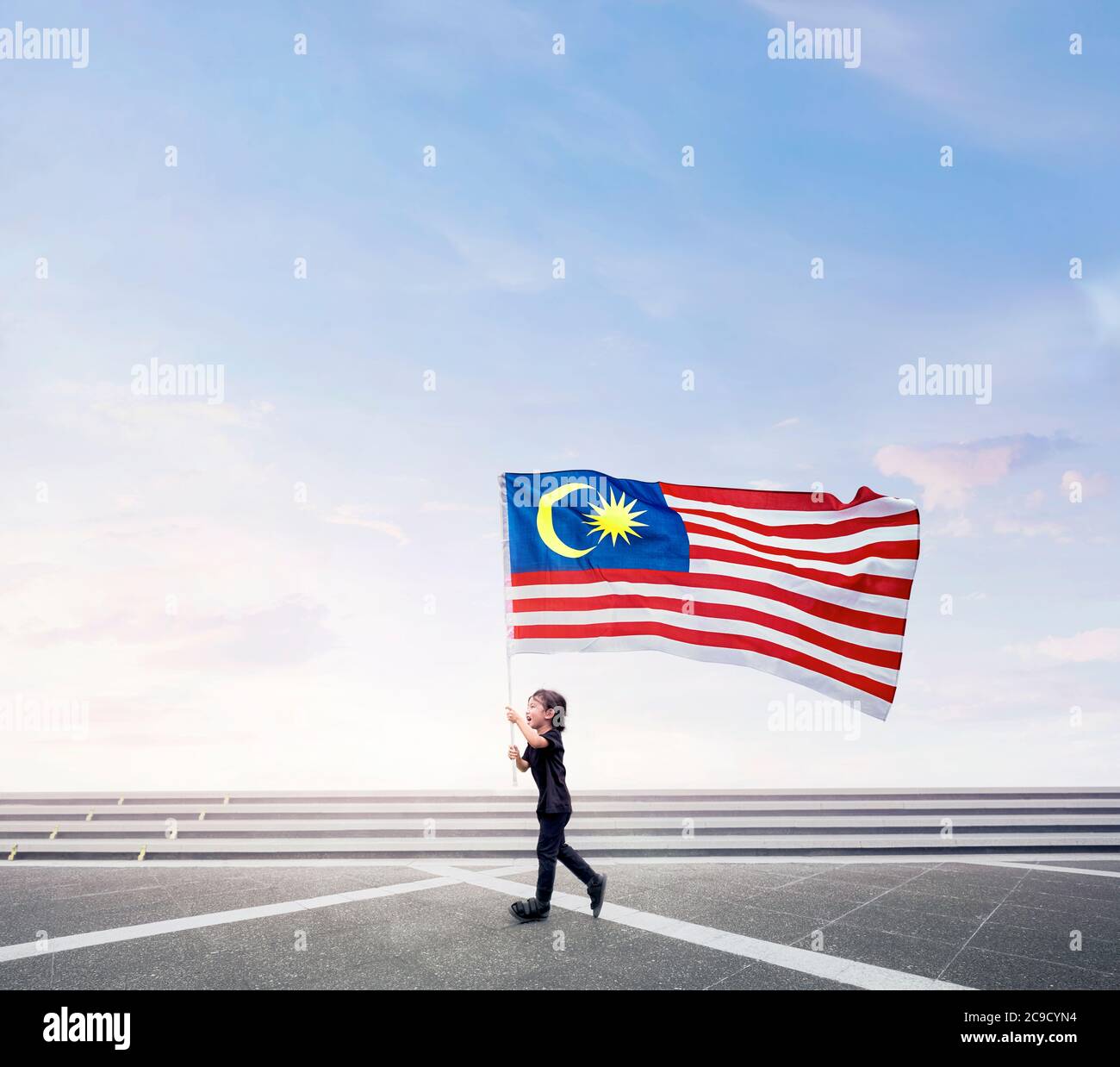 Joyeux garçon qui court tout en tenant le drapeau de Malaisie sur l'espace ouvert. Bonne journée nationale. Banque D'Images