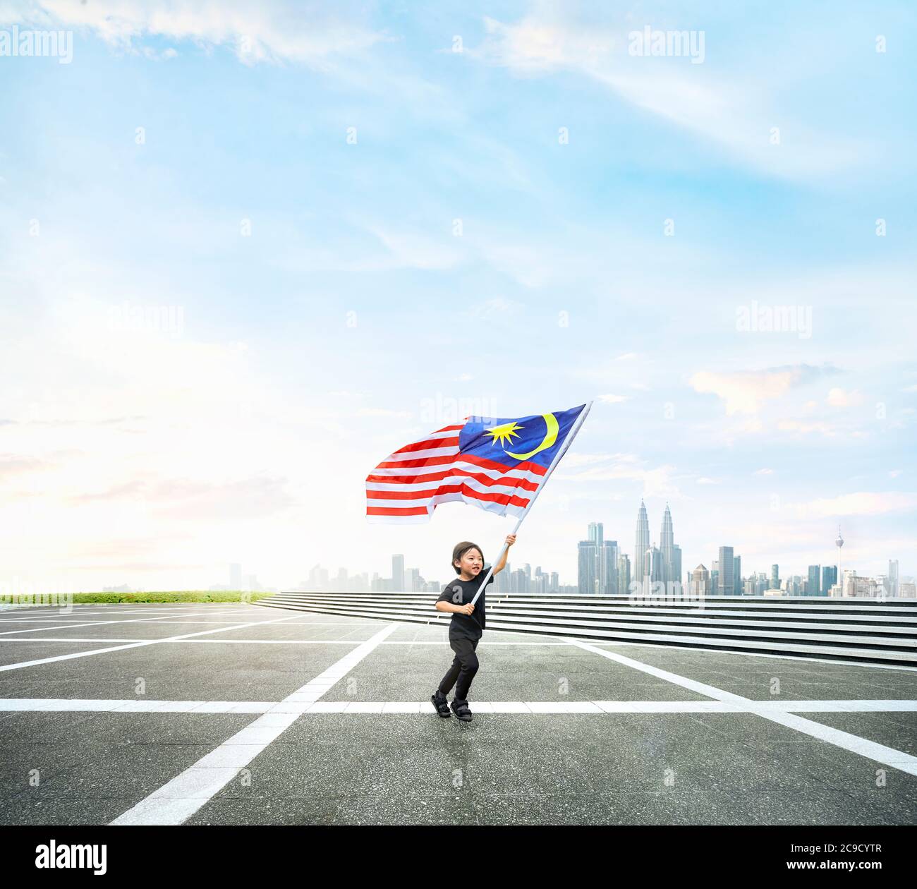 Joyeux garçon en train de courir tout en tenant le drapeau de Malaisie sur l'espace ouvert avec Kuala Lumpur paysage urbain. Banque D'Images