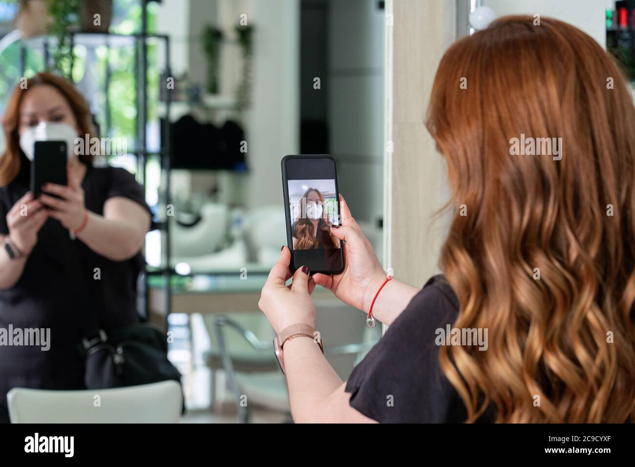 Jeune coiffeur client protégé par un masque facial, prenant un selfie de son nouveau look devant le mirrow. Nouvelle normalité Banque D'Images