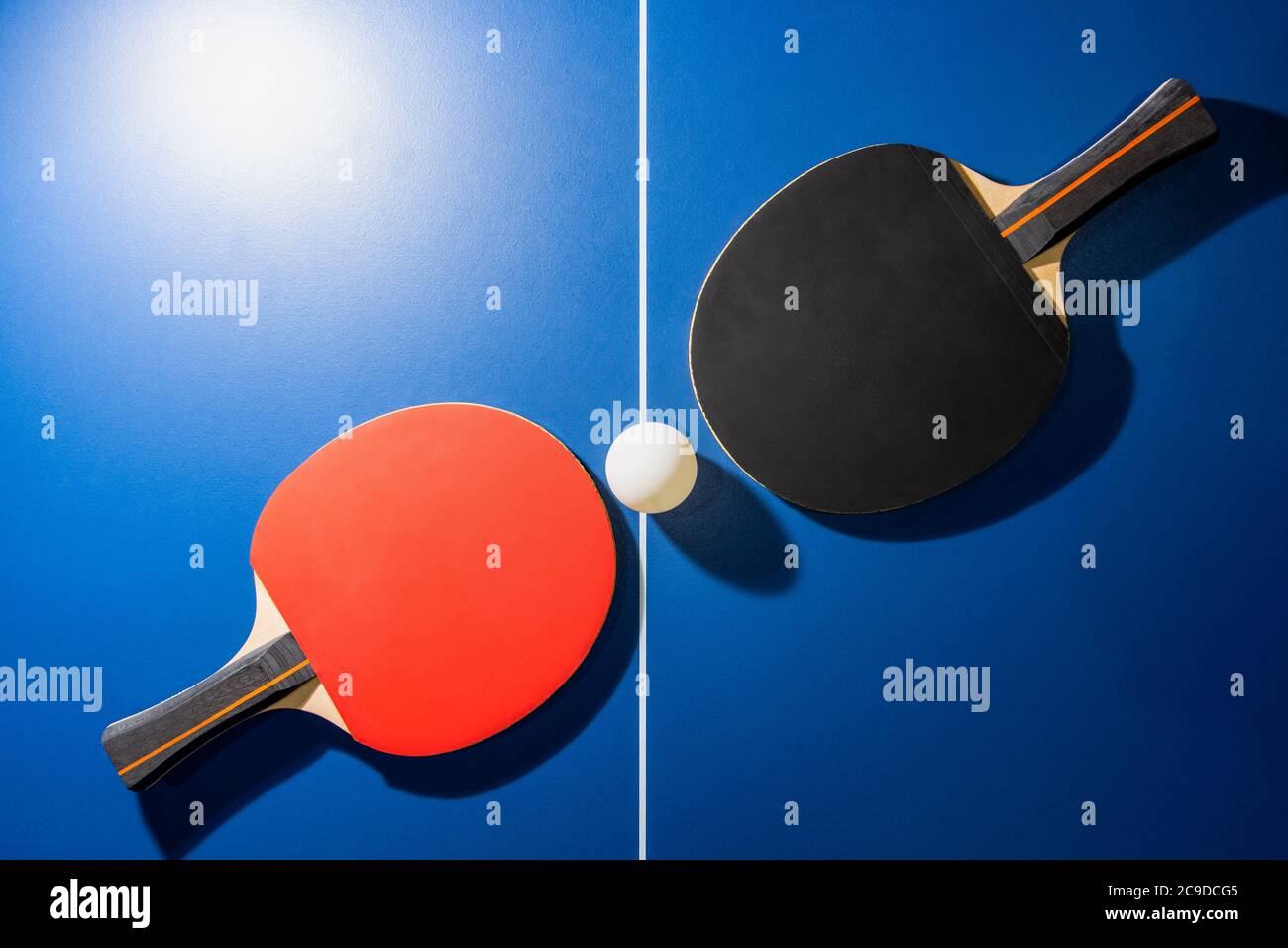 Vue de dessus une raquette de ping-pong noir et rouge et une balle de ping-pong blanche sur la table de ping-pong bleue avec un spot lumineux, deux paddle de ping-pong est Banque D'Images